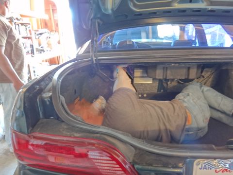 1993 Ford Taurus - Someone is working inside the trunk of a car, with another person standing by.