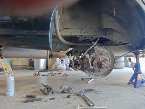 1993 Ford Taurus - The rear suspension and brake assembly of a 1993 Ford Taurus is visible, with tools scattered on the garage floor.