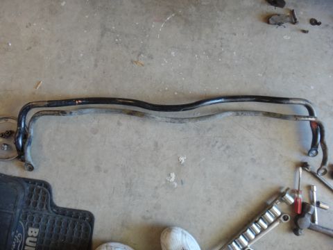 1993 Ford Taurus - Two sway bars are laid out on a concrete surface alongside various tools and a black floor mat.