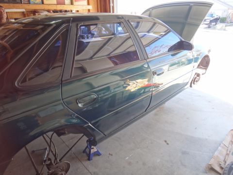 1993 Ford Taurus - Green 1993 Ford Taurus sedan with hood up, raised on jack stands for repairs in a garage.