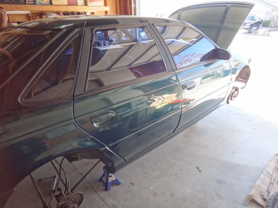 1993 Ford Taurus sedan on jack stands with hood open, undergoing maintenance in a garage