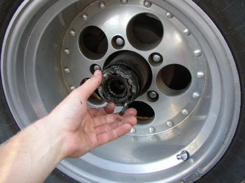 1989 Ford Bronco - A person is holding a disassembled manual locking hub assembly, with the wheel and tire visible in the background.