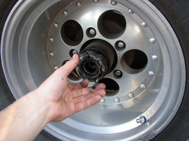 Hand holding greasy splined Warn hub part in front of polished 8-lug aluminum wheel