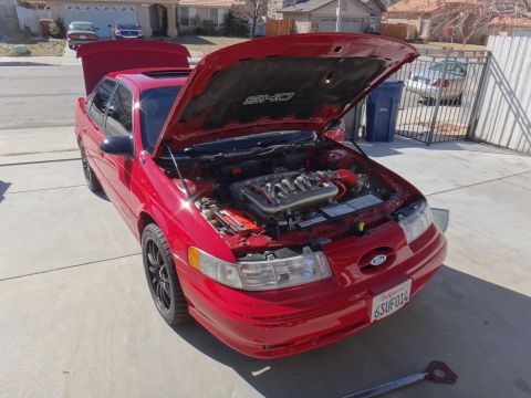 1993 Ford Taurus - The engine bay of a red 1993 Ford Taurus SHO is displayed with the hood fully open.