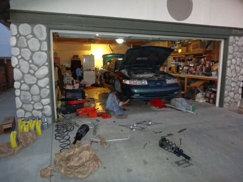 1993 Ford Taurus - Mechanic working on a 1993 Ford Taurus SHO in a garage, with suspension parts scattered around.