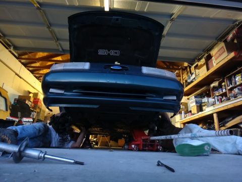 1993 Ford Taurus - A mechanic works on the underside of a 1993 Ford Taurus SHO in a garage.