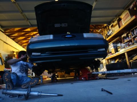 1993 Ford Taurus - Mechanic works on the underside of a 1993 Ford Taurus SHO in a garage setting.