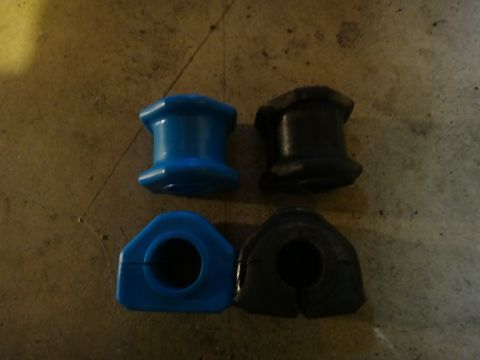 1993 Ford Taurus - Four suspension bushings, two new blue ones and two old black ones, are laid out on a concrete floor.