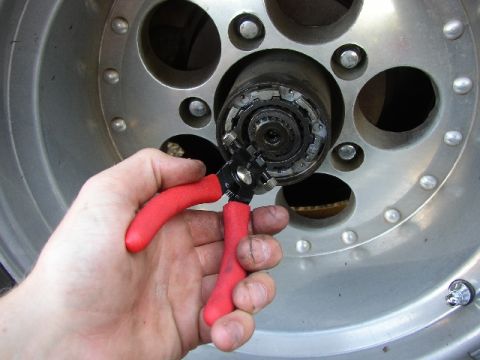 1989 Ford Bronco - Close-up of a hand working on a wheel hub with specialized pliers.
