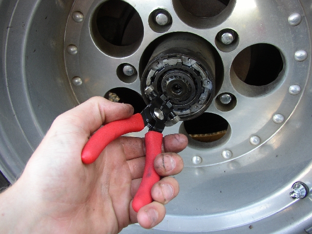Hand using red snap ring pliers on an exposed front wheel hub through an aluminum wheel