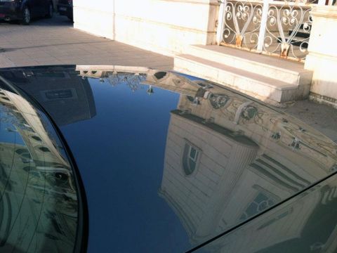 2001 Mercury Grand Marquis - The glossy surface of a car's roof reflects the surrounding architecture and a decorative gate.