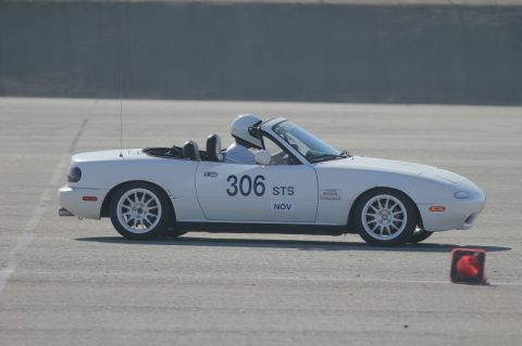 1991 Mazda Miata - A driver in a white 1991 Mazda Miata participates in a track event, indicated by the number on the door and safety equipment.