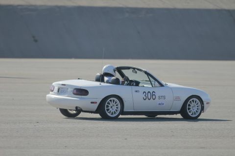 1991 Mazda Miata - A white 1991 Mazda Miata, identified by its distinctive body style, competes on a flat, open course.