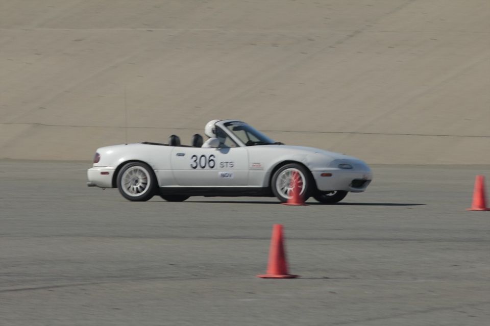 White 1991 Mazda Miata with number 306 on the door, driving on a track with orange cones