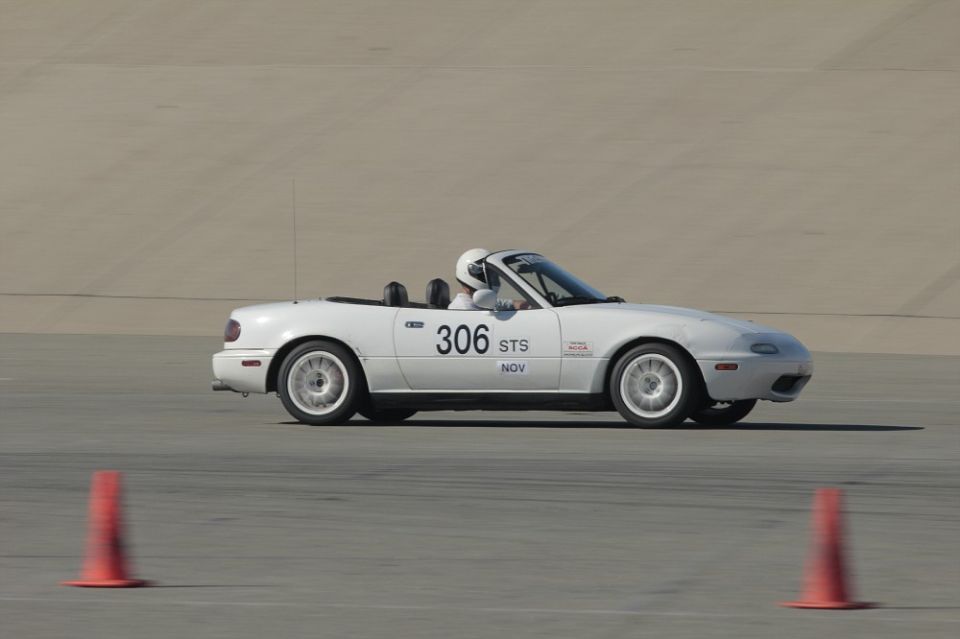 White convertible sports car with racing numbers '306 STS NOV' on the side, seen from the side at a track