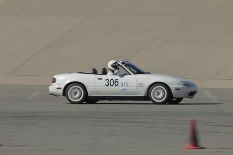 1991 Mazda Miata - A white 1991 Mazda Miata, identified by its distinctive body style and racing number 306 STS, is captured in profile on a track.