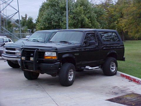 1995 Ford Bronco - A black Ford Bronco is parked next to a Chevrolet pickup truck on a paved lot.
