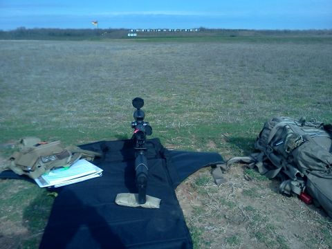 1996 Ford Bronco - A rifle scope is positioned on a mat at a shooting range, with gear scattered around the grassy field.