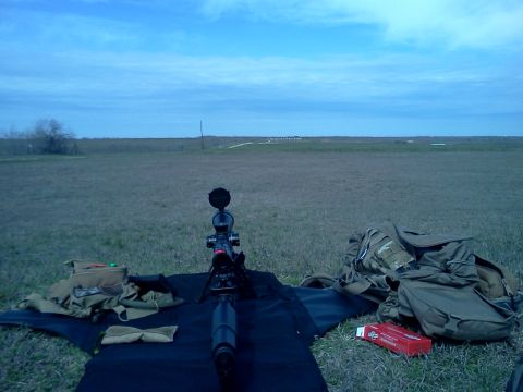 1996 Ford Bronco - A rifle scope and bipod are set up on a mat in an open field, with tactical gear nearby.