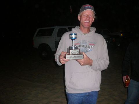 1988 Ford Bronco - A man proudly holds a trophy, with a white SUV visible in the dimly lit background.