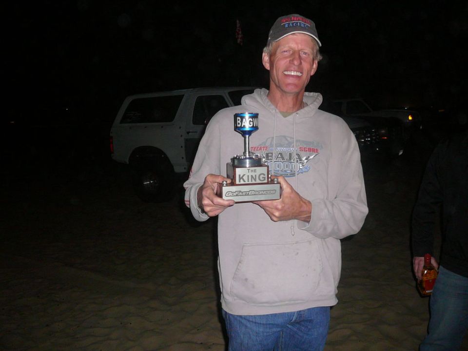 Man holding a trophy with a white SUV in the background at night