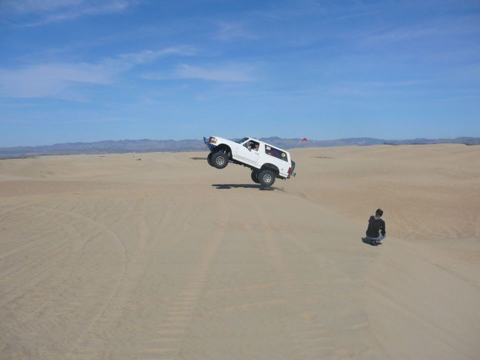 White 1988 Ford Bronco airborne over sand dunes