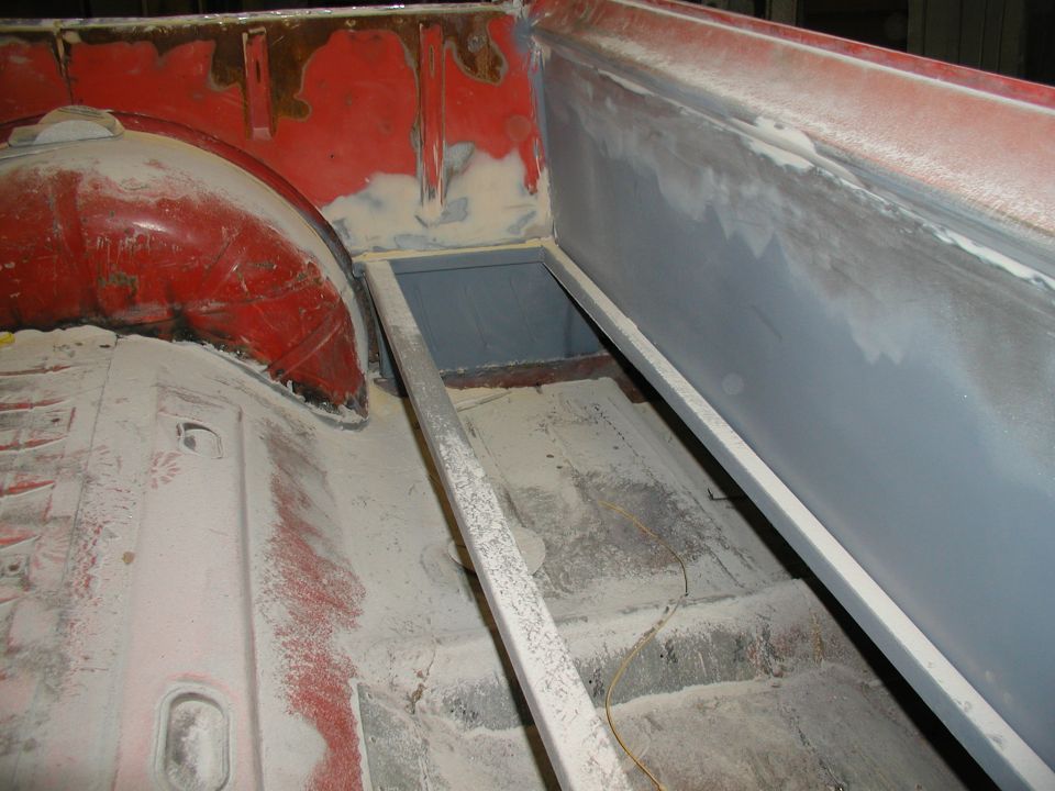 Truck bed interior with red paint, primer, and body filler visible. Metal bracing runs along the bed floor