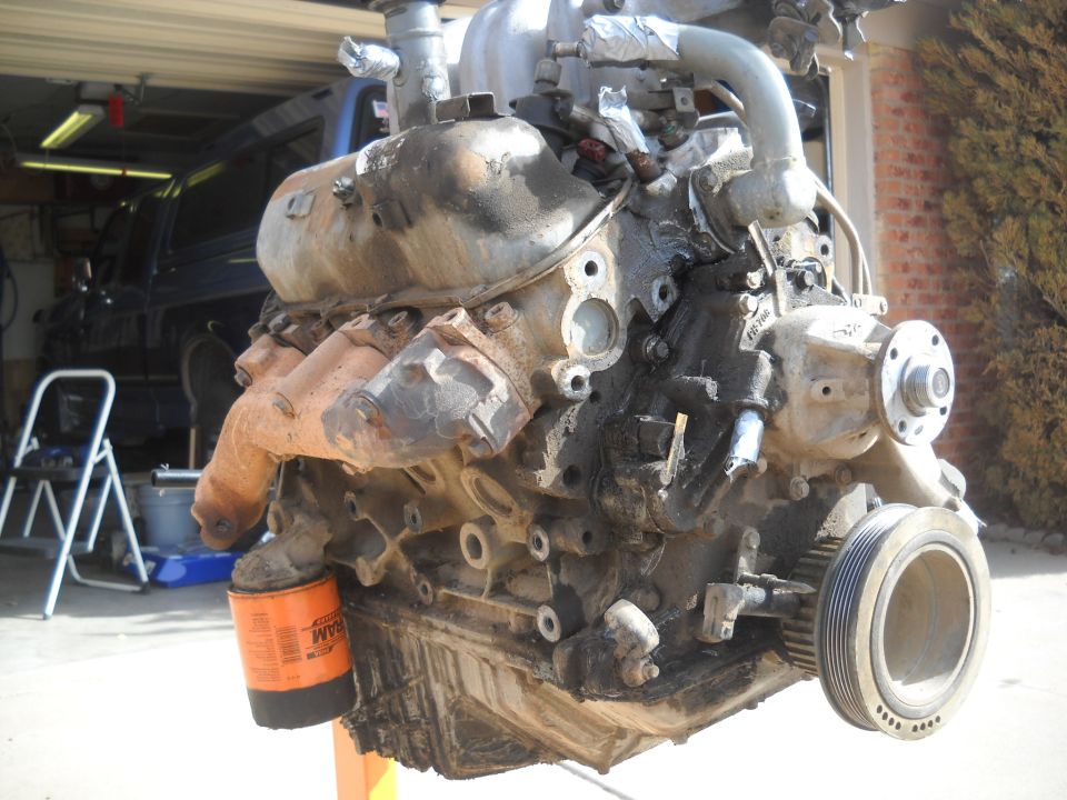 Engine on an orange stand, with an oil filter attached. A blue SUV is visible in the background