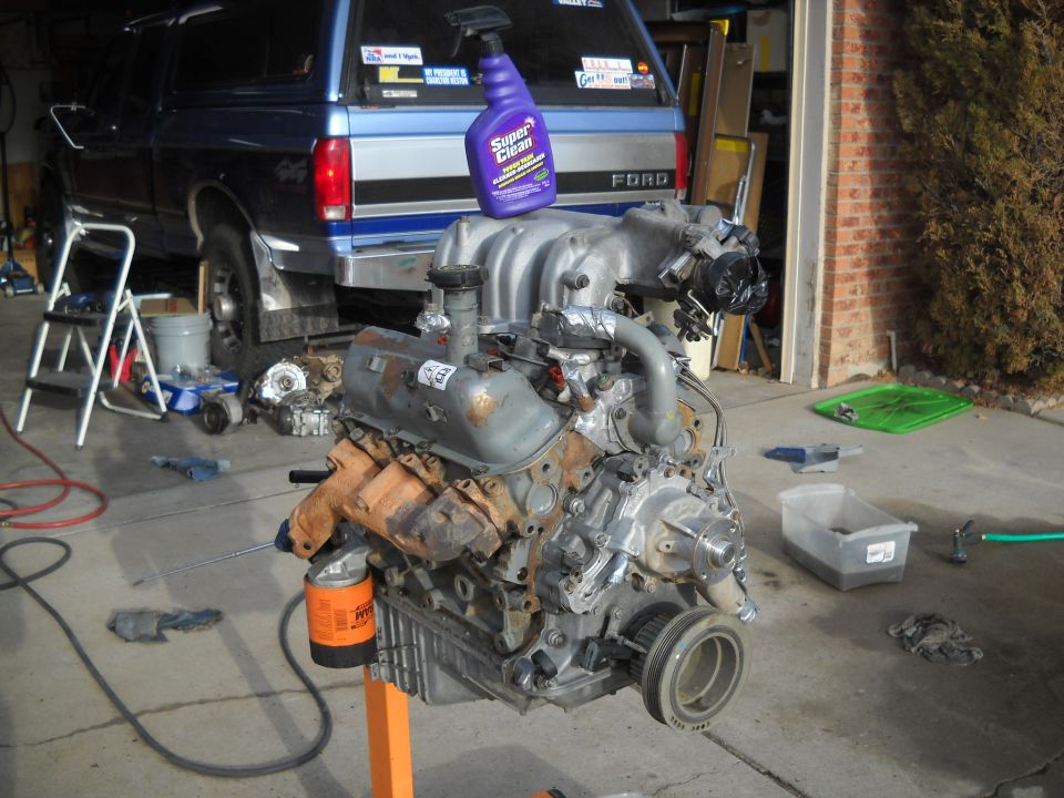 V8 engine on an orange engine stand, with a blue Ford truck in the background