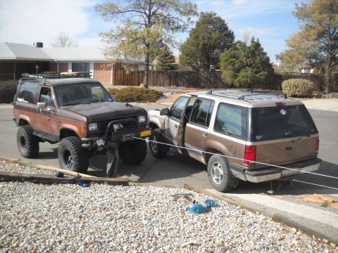1992 Ford Explorer - Two SUVs are parked in a residential driveway, one is significantly modified with a lift kit and winch.