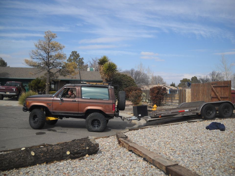 Brown Ford Bronco II towing a trailer, side view, lifted suspension, spare tire on rear
