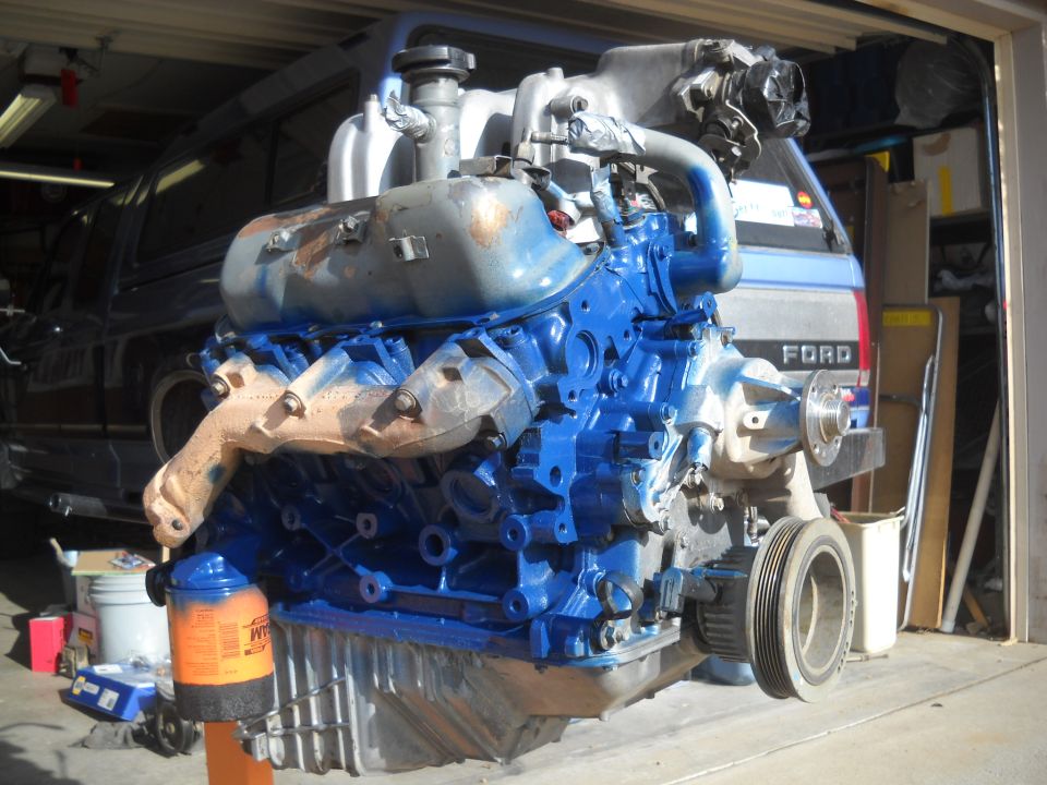 Blue painted V8 engine on an orange stand, with a Ford truck in the background