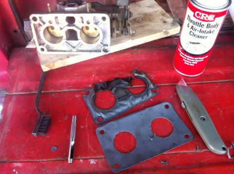 1989 Ford Bronco - Carburetor parts and cleaning supplies laid out on a red surface for maintenance.