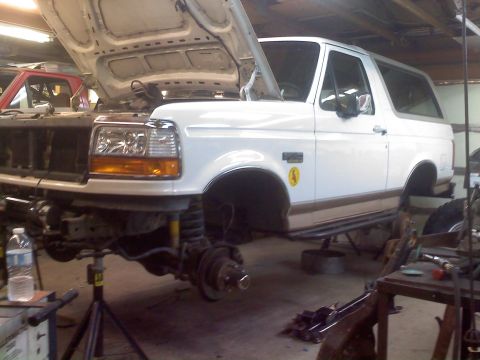 1996 Ford Bronco - A white 1996 Ford Bronco is being worked on in a garage, with its front end lifted and disassembled.