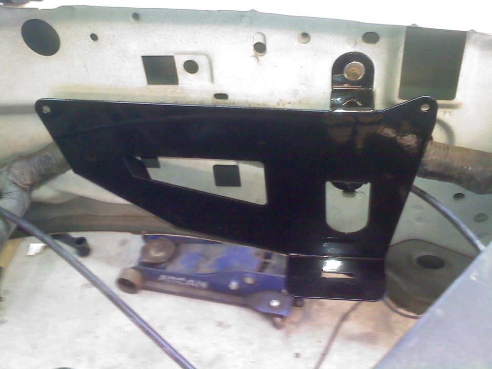 Engine bay with black metal bracket and blue hydraulic jack underneath