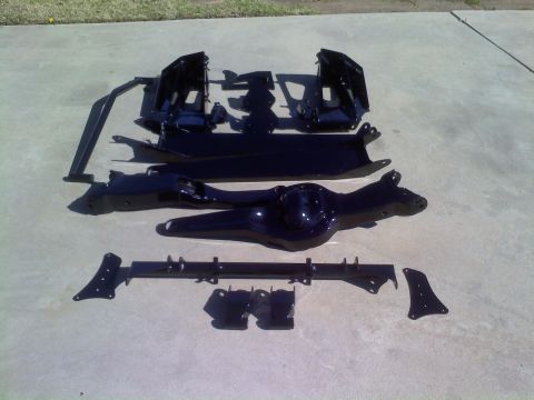 1996 Ford Bronco - Various black suspension parts, including a differential housing and frame pieces, are arranged on a concrete surface.