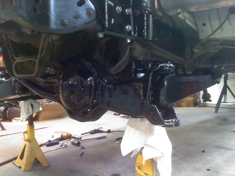 Undercarriage of a vehicle on jack stands, showing a black painted differential and suspension components
