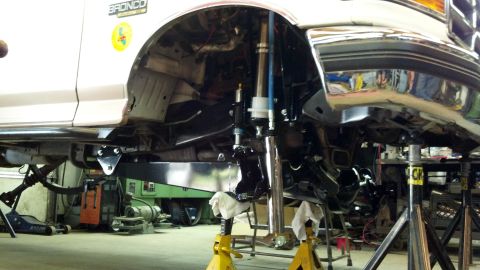 1996 Ford Bronco - White Ford Bronco undergoing suspension modifications in a garage.