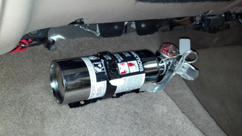 1996 Ford Bronco - Fire extinguisher with gauge mounted on the carpeted floor of a vehicle's interior.
