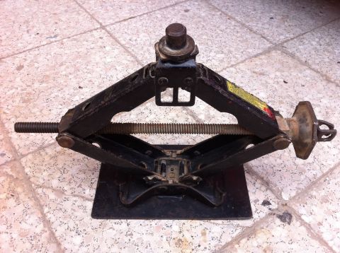 1998 Ford Crown Victoria - A black scissor jack is shown on a tiled surface, with a yellow warning sticker visible.