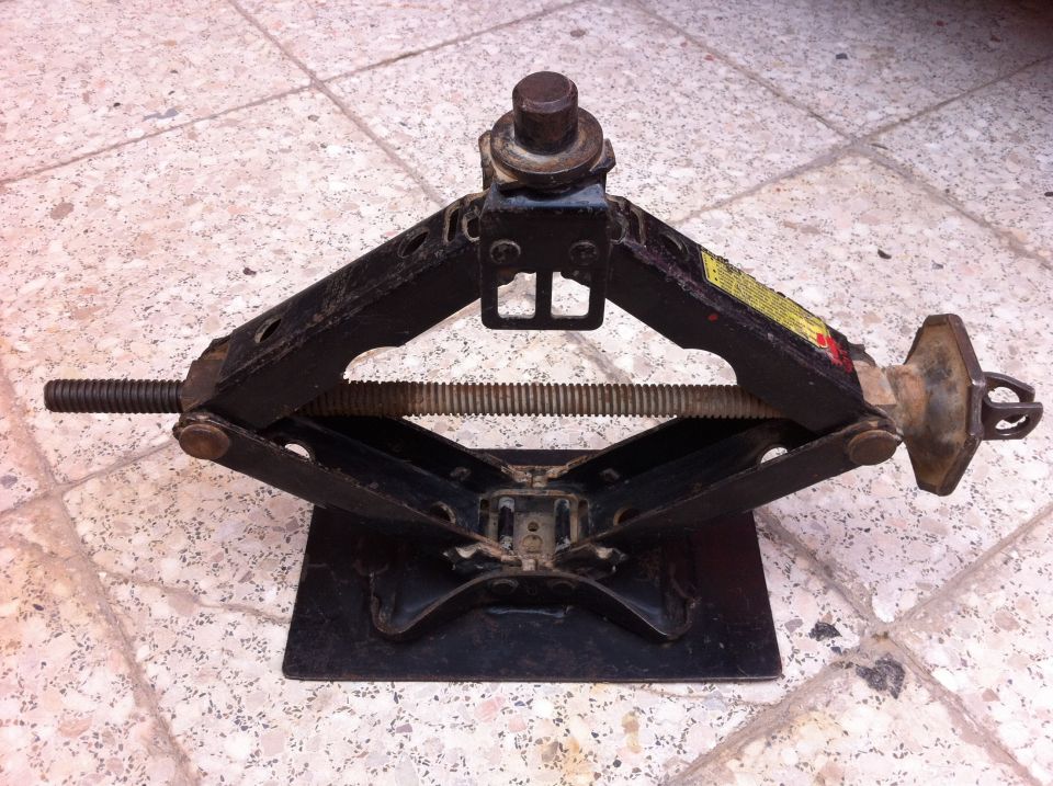 Black scissor jack with a threaded rod and yellow warning sticker