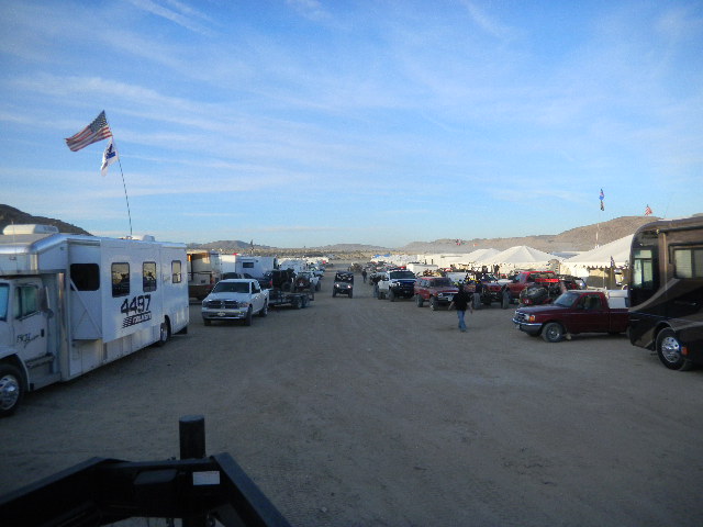 Desert scene with RV, trucks, and tents under a blue sky