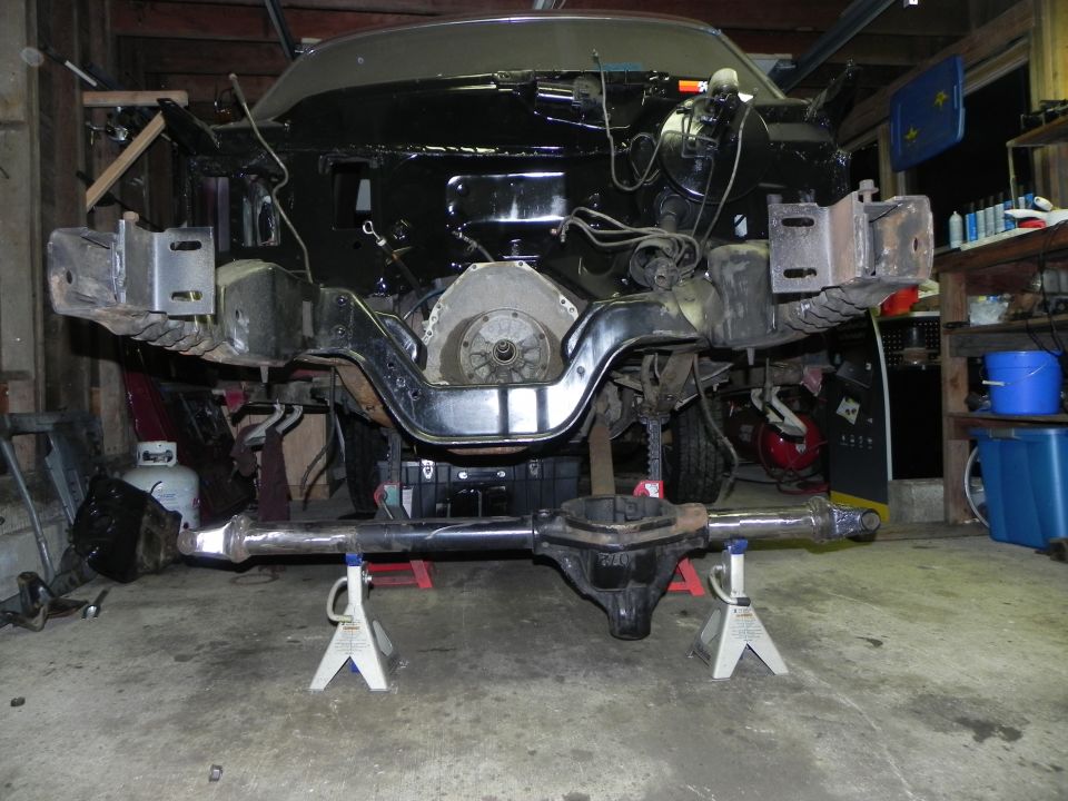 Vehicle frame on jack stands with engine and drivetrain parts exposed, undergoing modification