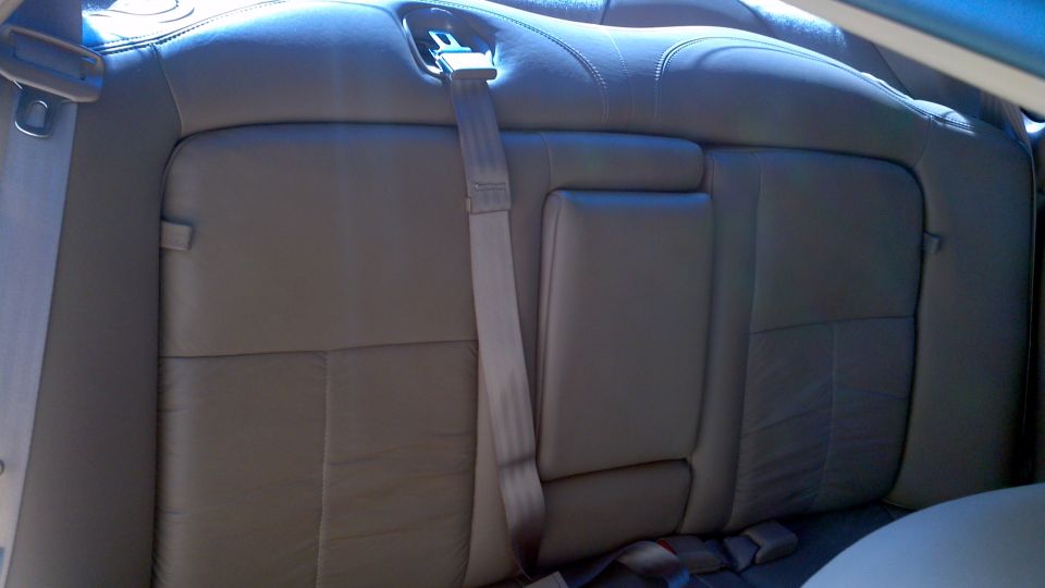 Back seat of a car with beige leather upholstery and a gray seatbelt