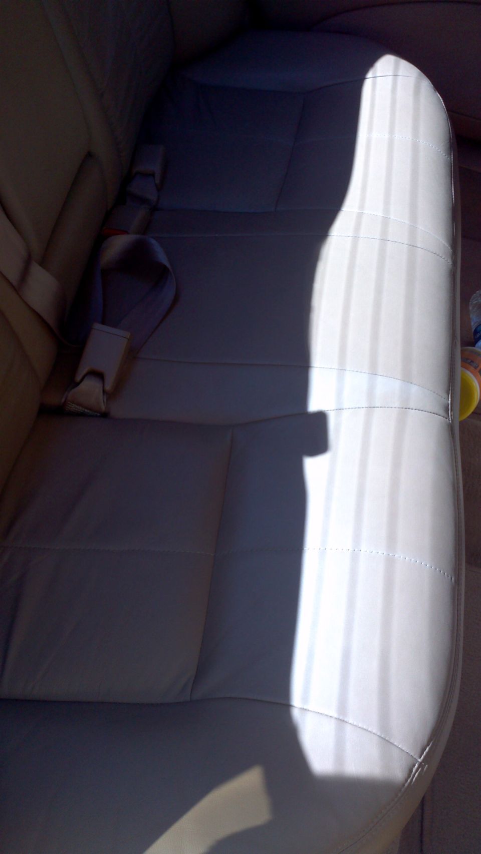 Car interior showing light-colored leather rear seats and seatbelts. A bright light casts a shadow across the seats