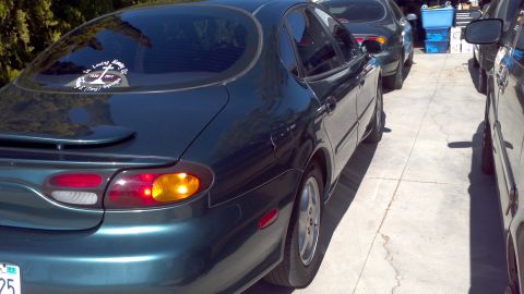 1996 Ford Taurus - A dark green 1996 Ford Taurus sedan is parked in a driveway next to other vehicles.
