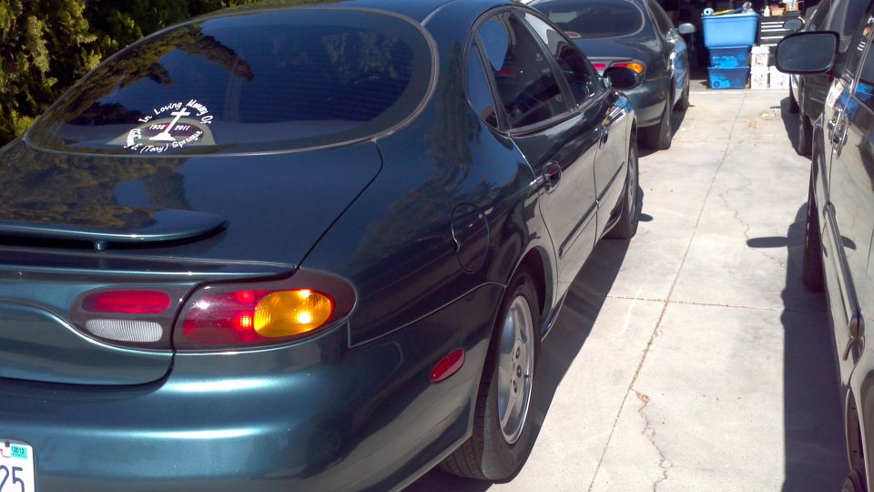 Dark green 1996 Ford Taurus sedan, rear view, with a spoiler and a sticker on the rear window