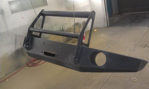 1995 Ford Bronco - Aftermarket bumper with brush guard is suspended for painting in a workshop environment.