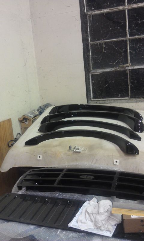 1995 Ford Bronco - Black fender flares and a grille are displayed on a car hood, possibly for a Ford Bronco, with a window in the background.