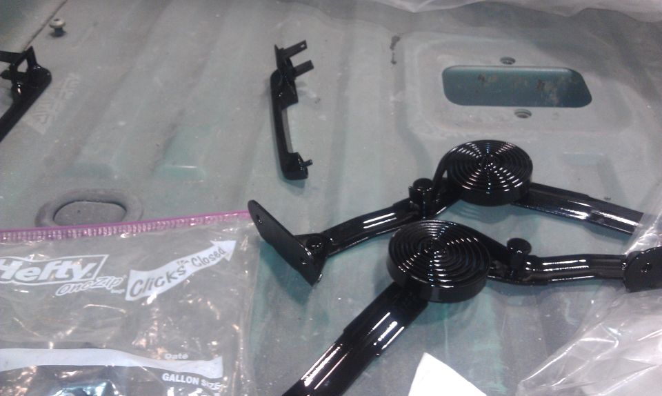 Two black spiral-design door handles and a black interior trim piece on a gray surface next to a Hefty bag